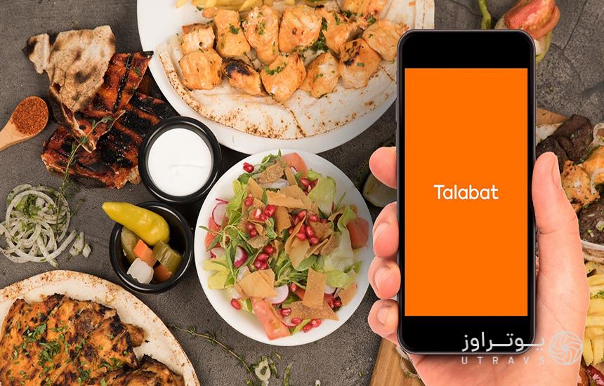 تصویری از اپلیکیشن سفارش غذا «talabat» دبی در یک گوشی و چند ظرف غذا در کنار آن
